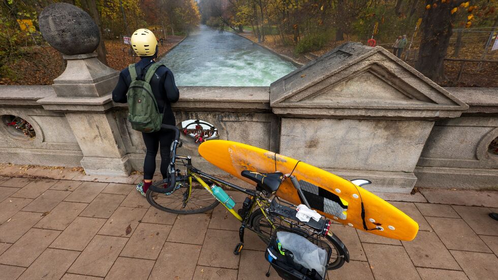 Ein Mann mit einem Surfboard an seinem Fahrrad schaut von einer Brücke auf die - nicht mehr vorhandene - Eisbachwelle im Englischen Garten. Ein Mann mit einem Surfboard an seinem Fahrrad schaut von einer Brücke auf die - nicht mehr vorhandene - Eisbachwelle im Englischen Garten.