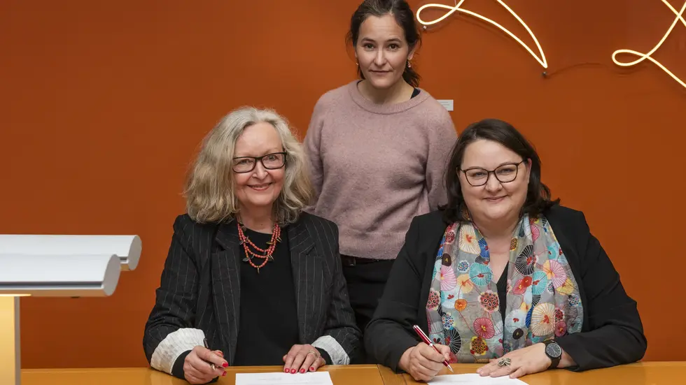Maraike Wittbrodt (links, Tochter von Ursula Winnington) und Katrin Stump (rechts, Generaldirektorin der SLUB) unterzeichnen den Schenkungsvertrag zur Übernahme des Nachlasses von Ursula Winnington. In der Mitte: Enkelin Lilly Böhm